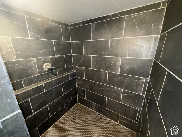 Shower with dark tiled walls, a built-in shower bench, a circular shower floor tile, and a wall-mounted shower head with a single handle control