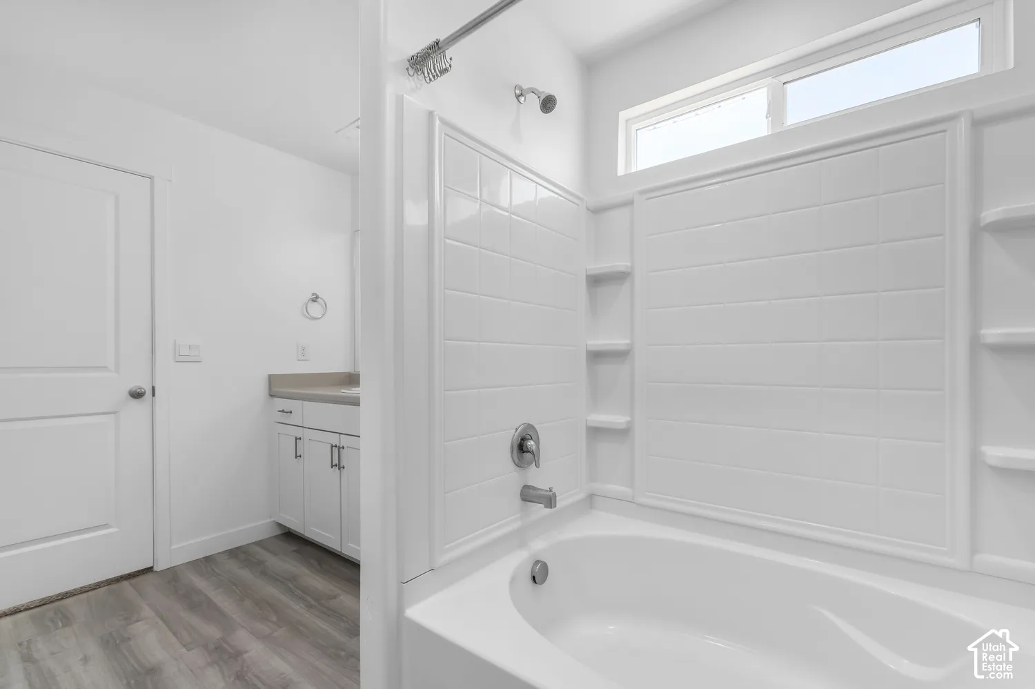 Bathroom featuring a tub-shower combination with tile-surround walls, wood-finish flooring, white cabinetry, and a transom window