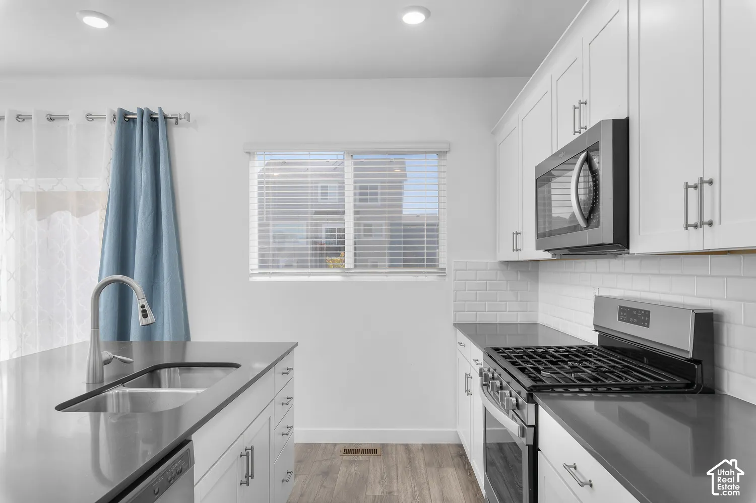 Kitchen featuring white shaker-style cabinetry, quartz countertops, subway tile backsplash, stainless steel gas range, and wood-finish flooring