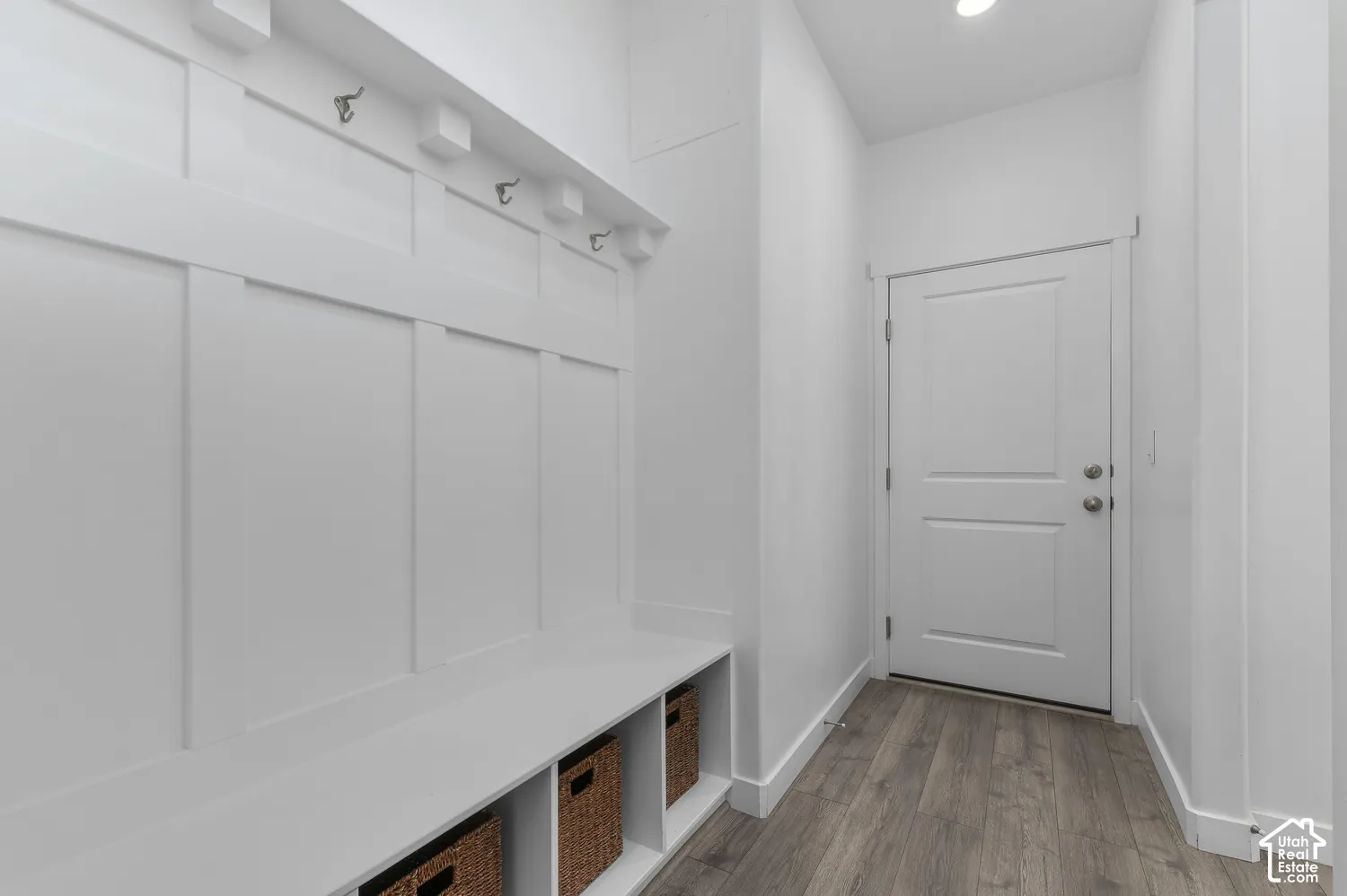 Built-in bench with integrated cubby storage, wall-mounted hardware hooks, white board-and-batten wainscoting, and wood-finish flooring