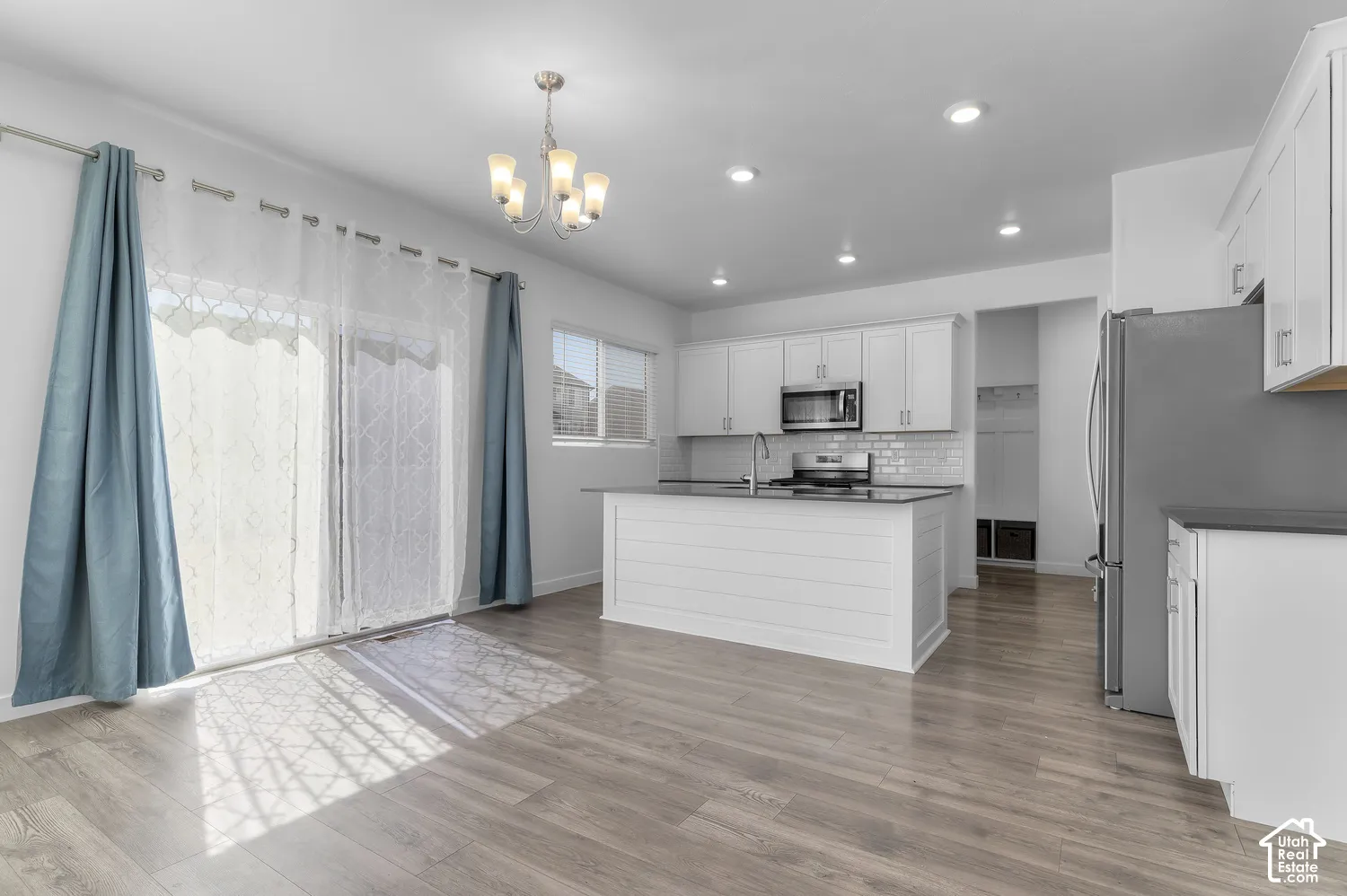Kitchen featuring white cabinetry, an island with shiplap detailing, stainless steel appliances, a tile backsplash, and wood-finish flooring