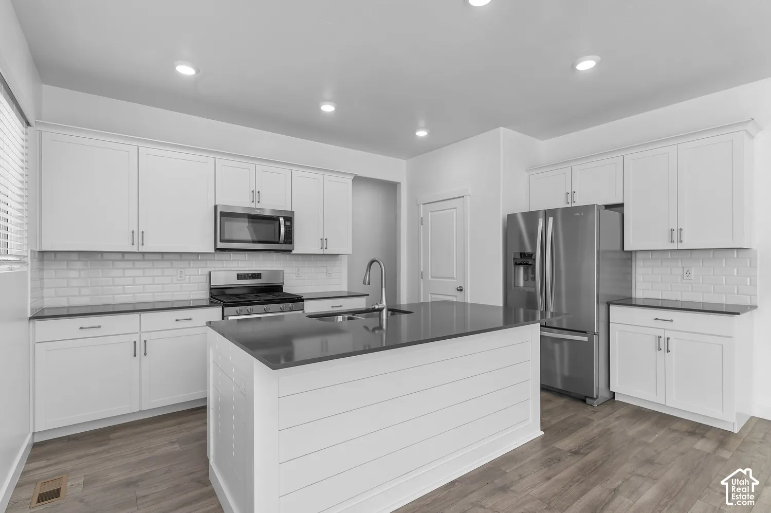 Kitchen featuring white shaker-style cabinetry, a center island with shiplap detailing, stone countertops, a white subway tile backsplash, and wood-finish flooring