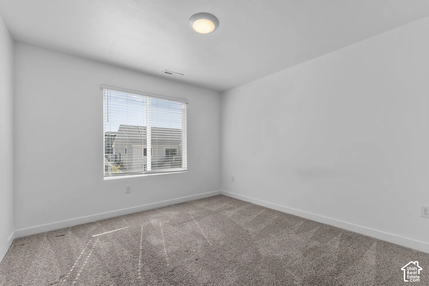 Neutral-toned wall-to-wall carpeting, crisp white walls, and a recessed ceiling light fixture, accented by a window with integrated blinds