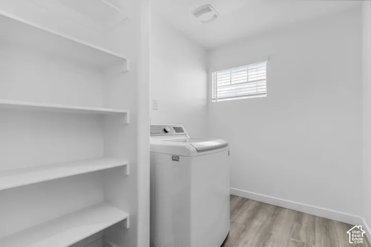 Dedicated laundry area featuring built-in white shelving, wood-finish flooring, and a window with blinds