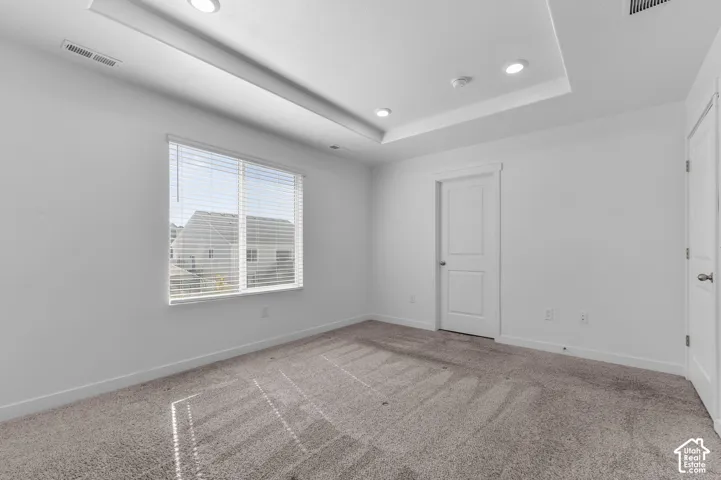Interior room featuring a tray ceiling, recessed lighting, carpeted flooring, and a window with integrated blinds