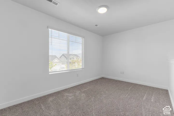 Neutral-toned wall-to-wall carpeting, crisp white walls, flush-mount ceiling lighting, and large window with horizontal blinds