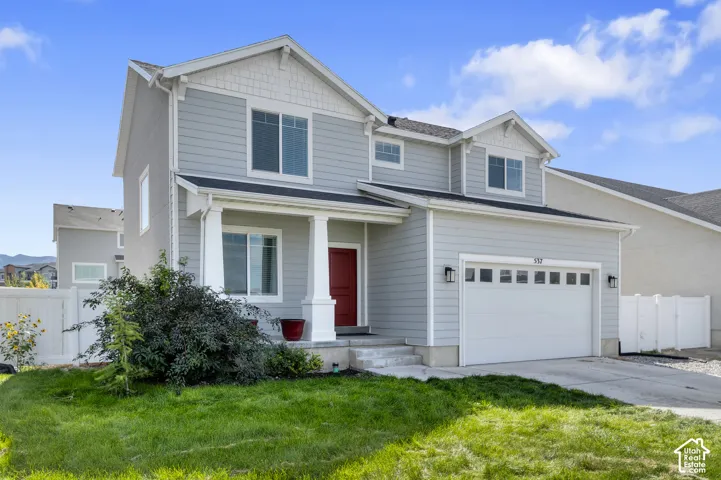 Two-story exterior featuring horizontal siding, decorative gable shingles, a covered front porch with square columns, and an attached two-car garage