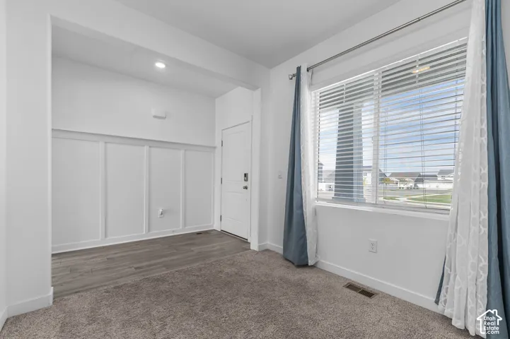 Interior space featuring board-and-batten wall detailing, wood-finish flooring, wall-to-wall carpeting, and a multi-pane window with adjustable blinds