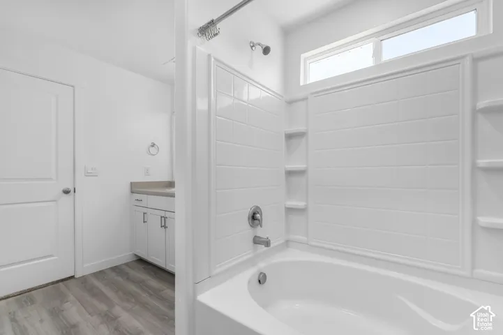 Bathroom featuring a tub-shower combination with tile-surround walls, wood-finish flooring, white cabinetry, and a transom window