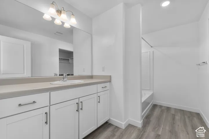 White cabinetry with brushed nickel hardware, expansive vanity mirror, integrated sink, and wood-finish flooring