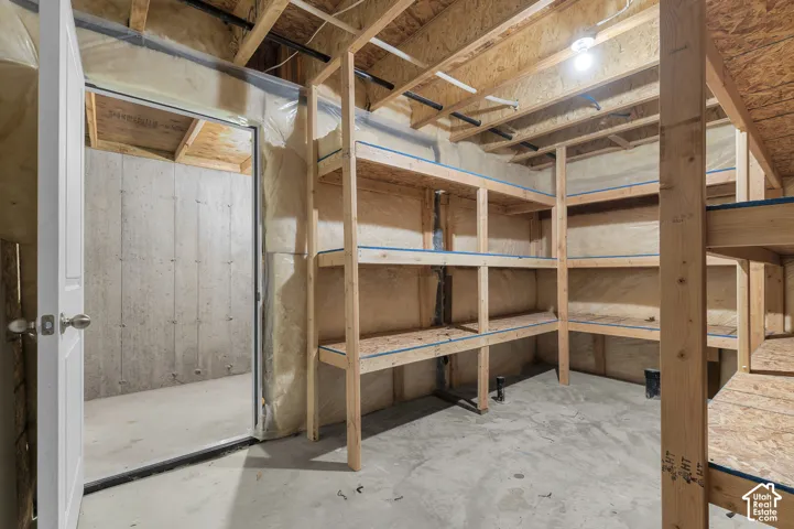 Unfinished storage area featuring concrete flooring, concrete foundation walls, and custom built-in wooden shelving units