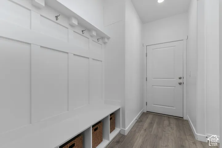 Built-in bench with integrated cubby storage, wall-mounted hardware hooks, white board-and-batten wainscoting, and wood-finish flooring