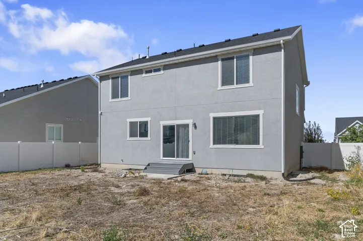 Two-story residence with stucco exterior, dark shingle roof, white vinyl perimeter fencing, and a sliding glass rear door with a small landing