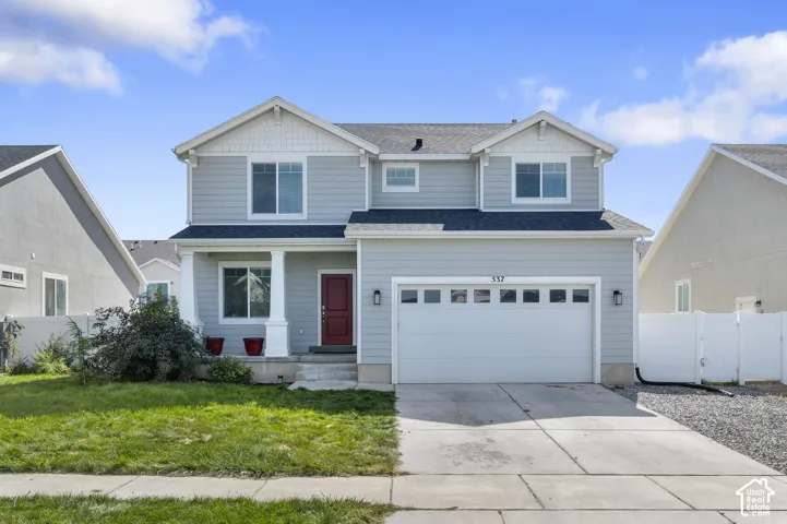Two-story residence featuring light blue horizontal siding, white trim accents, a front porch with decorative column, a two-car garage, and shake-style siding detailing on the upper gables