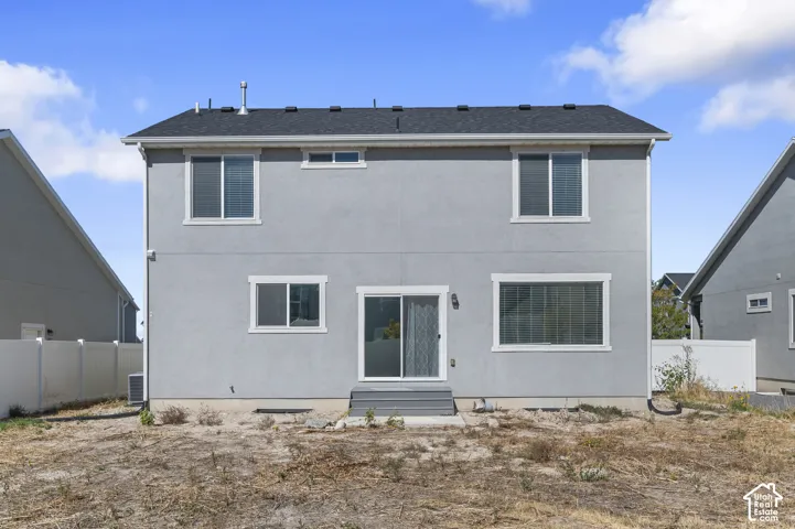 Two-story exterior featuring light gray stucco siding, asphalt shingle roofing, sliding glass door, and white vinyl privacy fencing