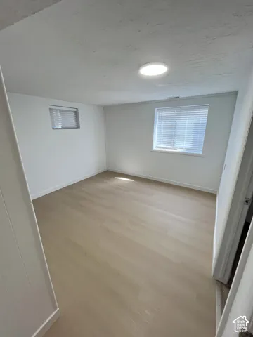 Light-filled room featuring wood-finish flooring, two windows with horizontal blinds, and a flush-mount overhead light fixture