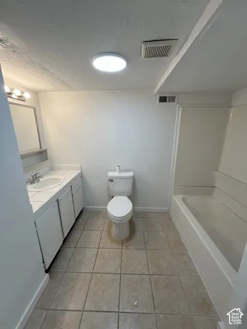 Bathroom featuring tile flooring, a white vanity with an integrated basin and countertop, a wall-mounted mirror, and a full-length tub and shower combination with a surround