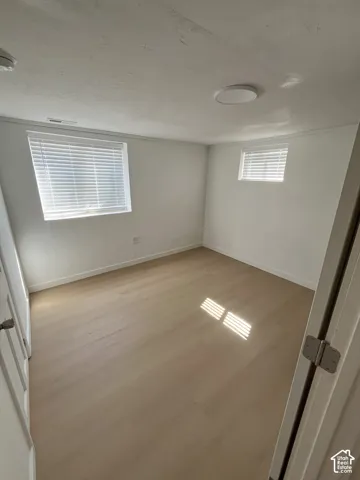Interior room featuring light-toned wood-finish flooring, white walls, two windows with horizontal blinds, and a flush-mount circular ceiling fixture