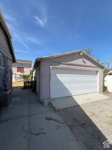 Detached garage with a paneled door, concrete driveway, and exterior wall-mounted light fixture