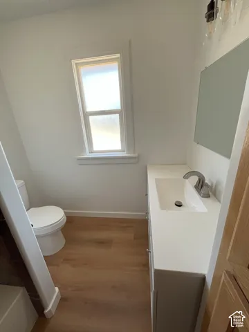 Bathroom featuring wood-finish flooring, a white vanity with an integrated rectangular sink, a brushed-nickel faucet, and a wall-mounted mirror