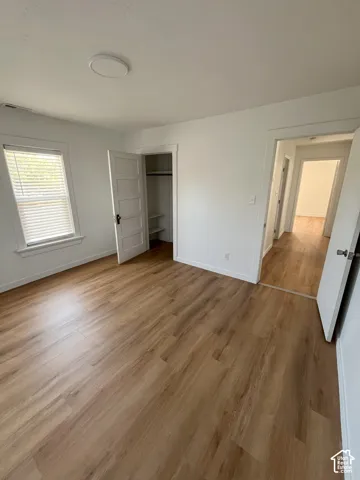 Interior space featuring wood-finish flooring, a multi-panel interior door, a built-in closet with integrated shelving, and a dual-pane window with horizontal blinds
