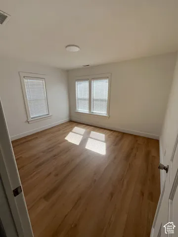 Room featuring wood-finish flooring, neutral walls, and three windows with white trim and blinds