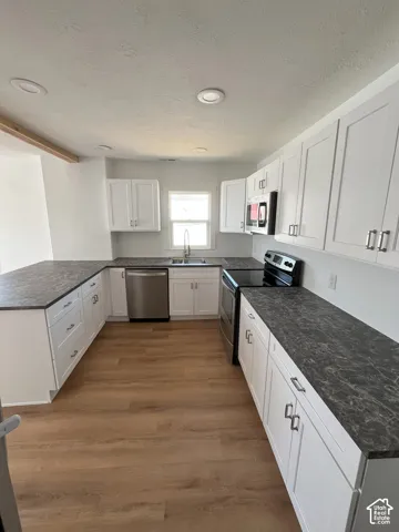 Kitchen featuring white shaker-style cabinetry, dark stone-finish countertops, stainless steel appliances, recessed ceiling lighting, and wood-finish flooring