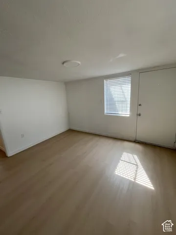 Neutral interior room featuring wood-finish flooring, a single window with horizontal blinds, and a flush-mount ceiling light fixture