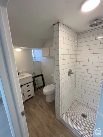 Walk-in shower featuring white subway tile walls and penny tile flooring, wood-finish tile flooring, white vanity cabinet with drawers, and wall-mounted cabinetry