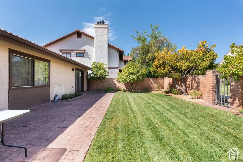Expansive lawn area, brick paver patio, mature trees, and a privacy wall with a wrought iron gate