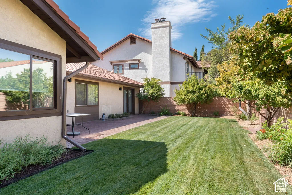 Expansive green lawn with a brick patio, mature trees, and a stucco exterior with tile roofing