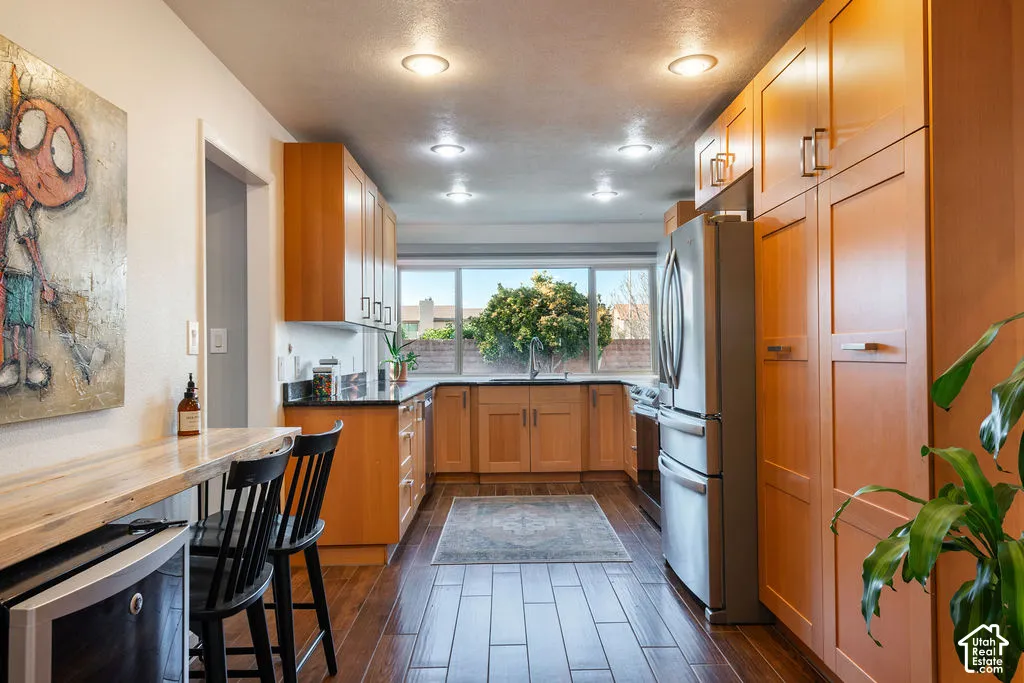 Kitchen featuring wood-finish flooring, recessed lighting, wood cabinetry, dark countertops, and stainless-steel appliances