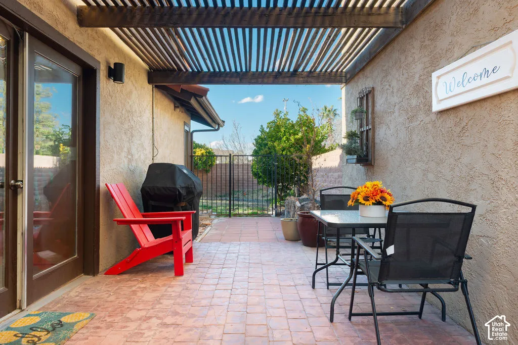Covered patio with a slatted pergola, textured stucco wall, and brick-patterned hardscaping