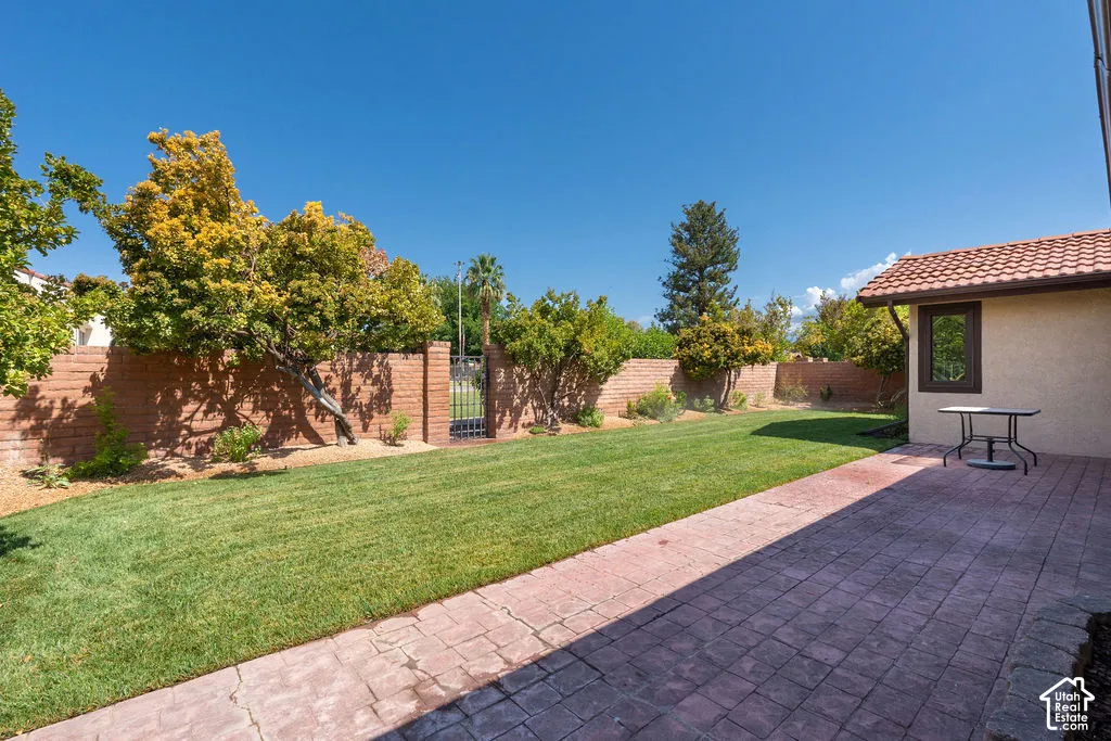 Expansive backyard featuring a manicured lawn, brick retaining wall, and a stamped concrete patio