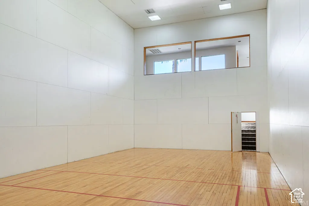 Indoor court featuring wood-finish flooring with red court lines, white panel walls, and upper windows with wood trim