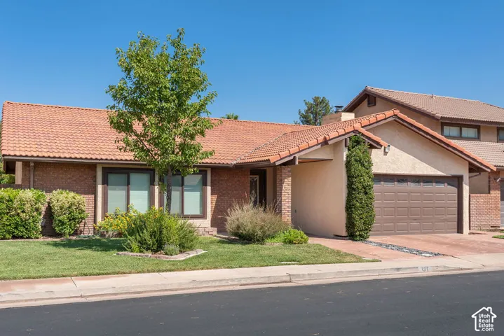 Terracotta tile roof, brick exterior, stucco siding, attached garage, and a manicured lawn