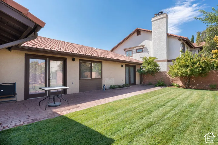 Expansive backyard featuring a brick paver patio, lush green lawn, and mature trees