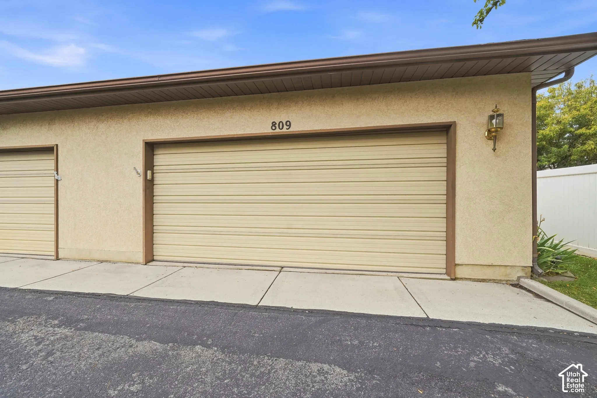 Stucco exterior garage with a wide sectional overhead door, concrete apron, and wall-mounted exterior sconce