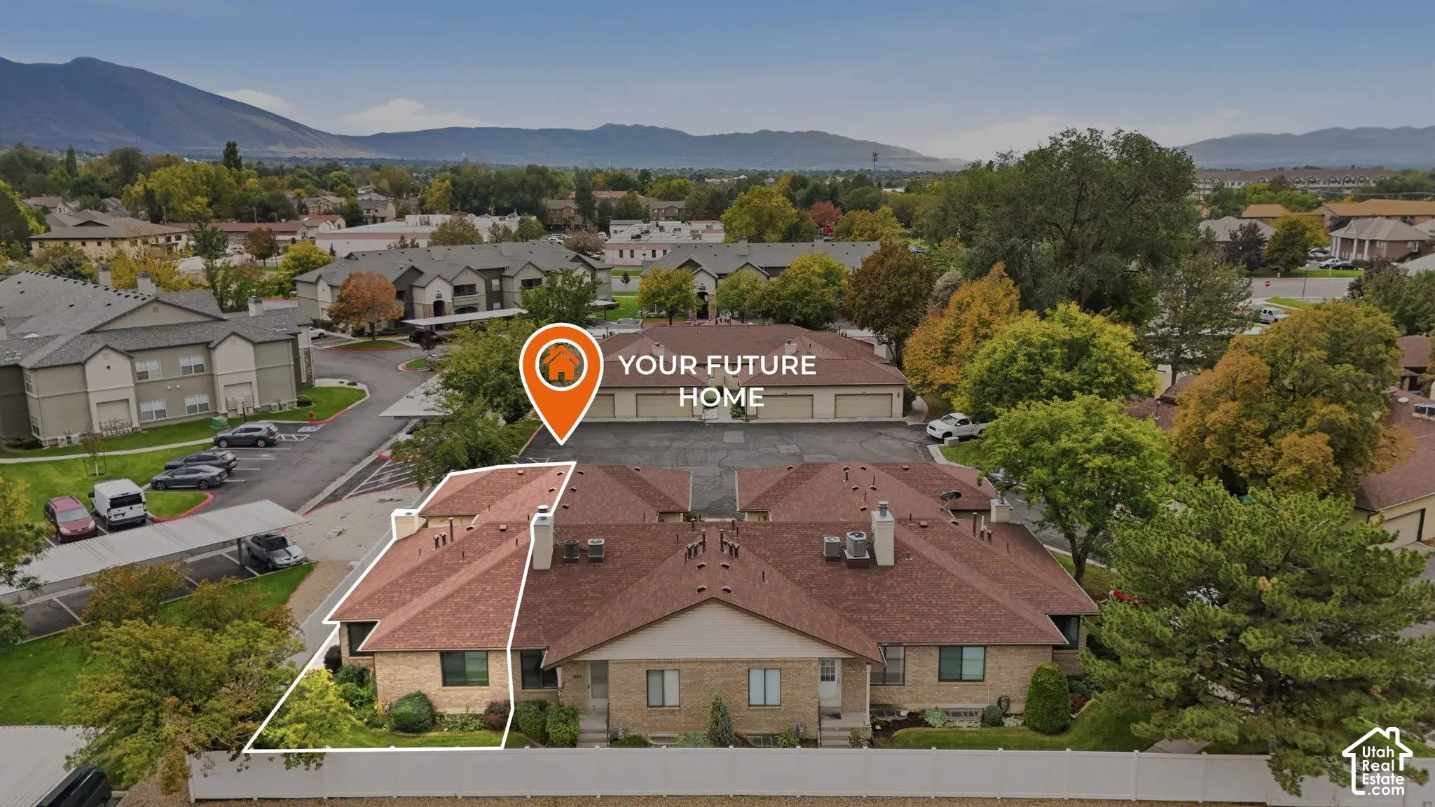 Aerial perspective of a multi-unit property featuring a multi-pitched shingled roof, light-toned masonry exterior, and established surrounding landscaping set against a mountain backdrop