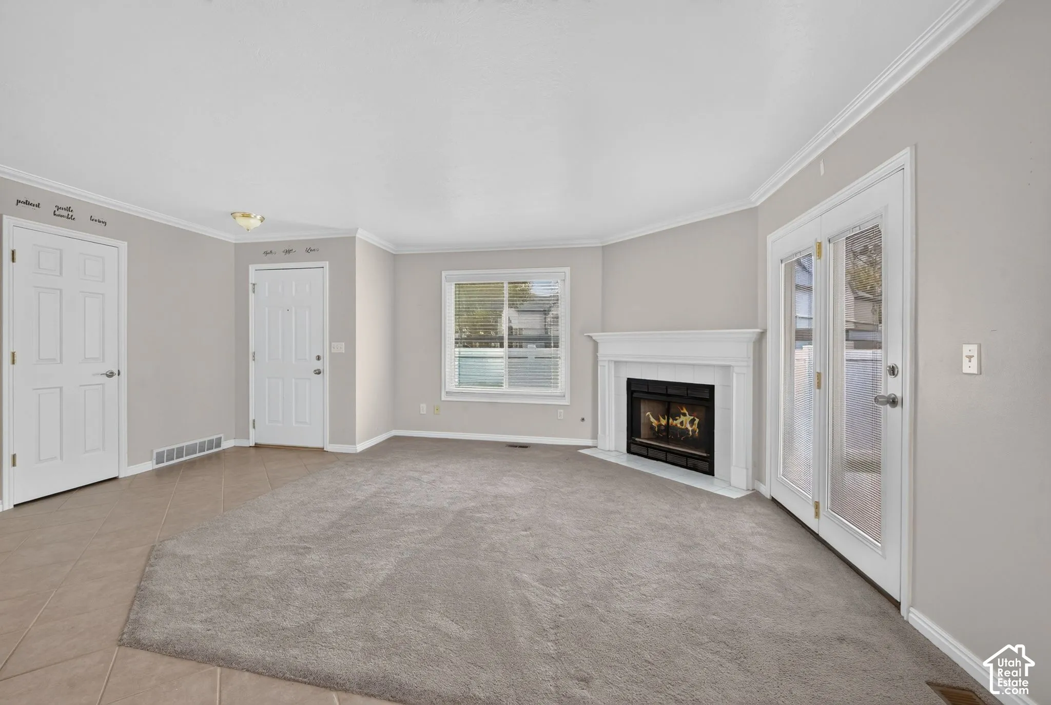 Neutral-toned room featuring a central fireplace with a white mantel, glass-paneled double doors, neutral carpeting, and tiled entry flooring