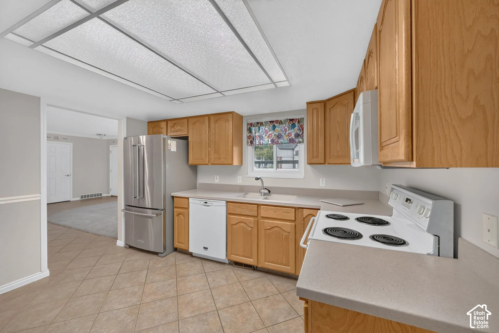 Kitchen featuring wood cabinetry, stainless steel refrigerator, white electric range, integrated dishwasher, and tile flooring