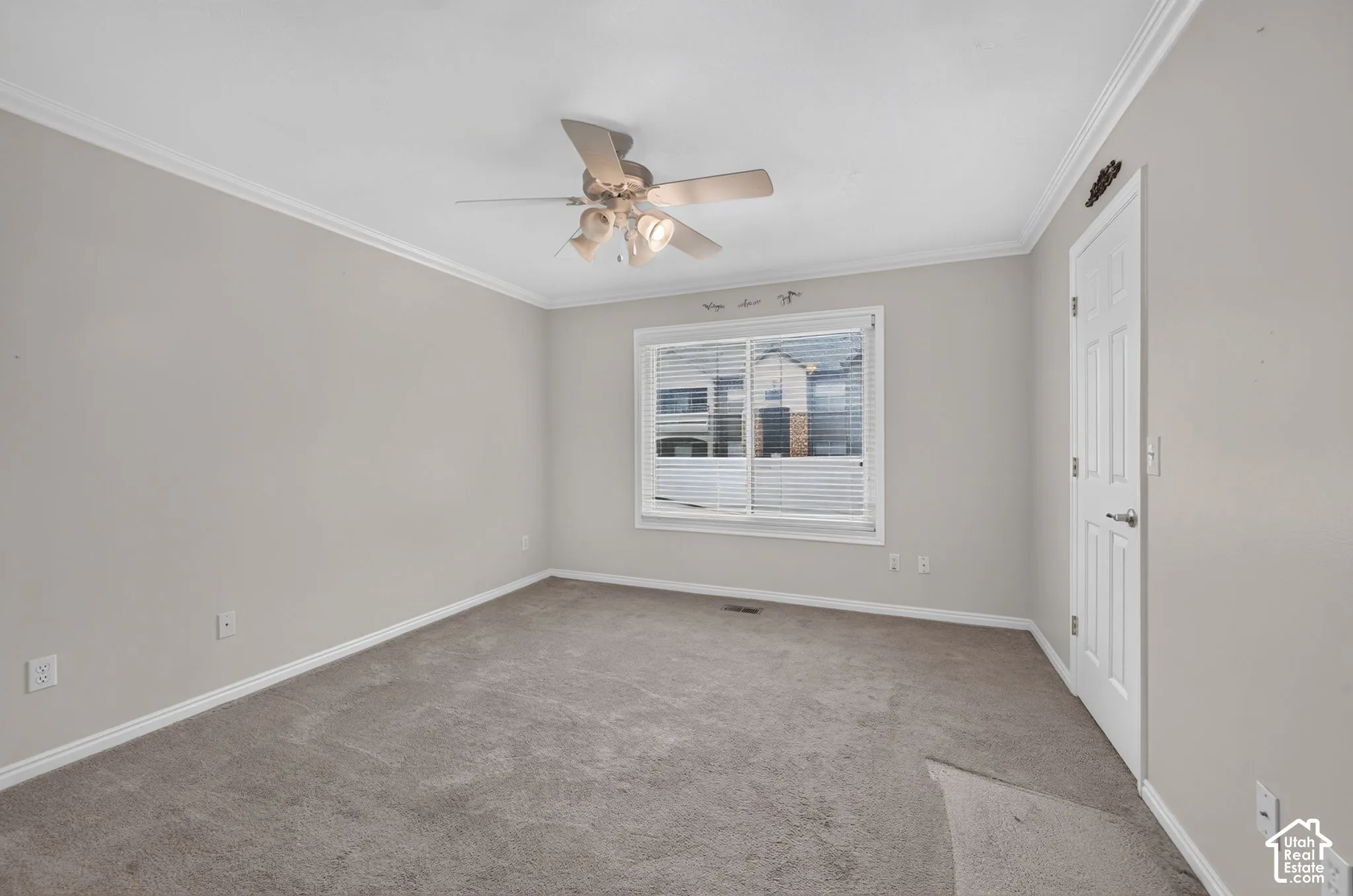 Neutral-toned interior featuring wall-to-wall carpeting, crown molding, a ceiling fan with integrated lighting, and a sliding window with horizontal blinds