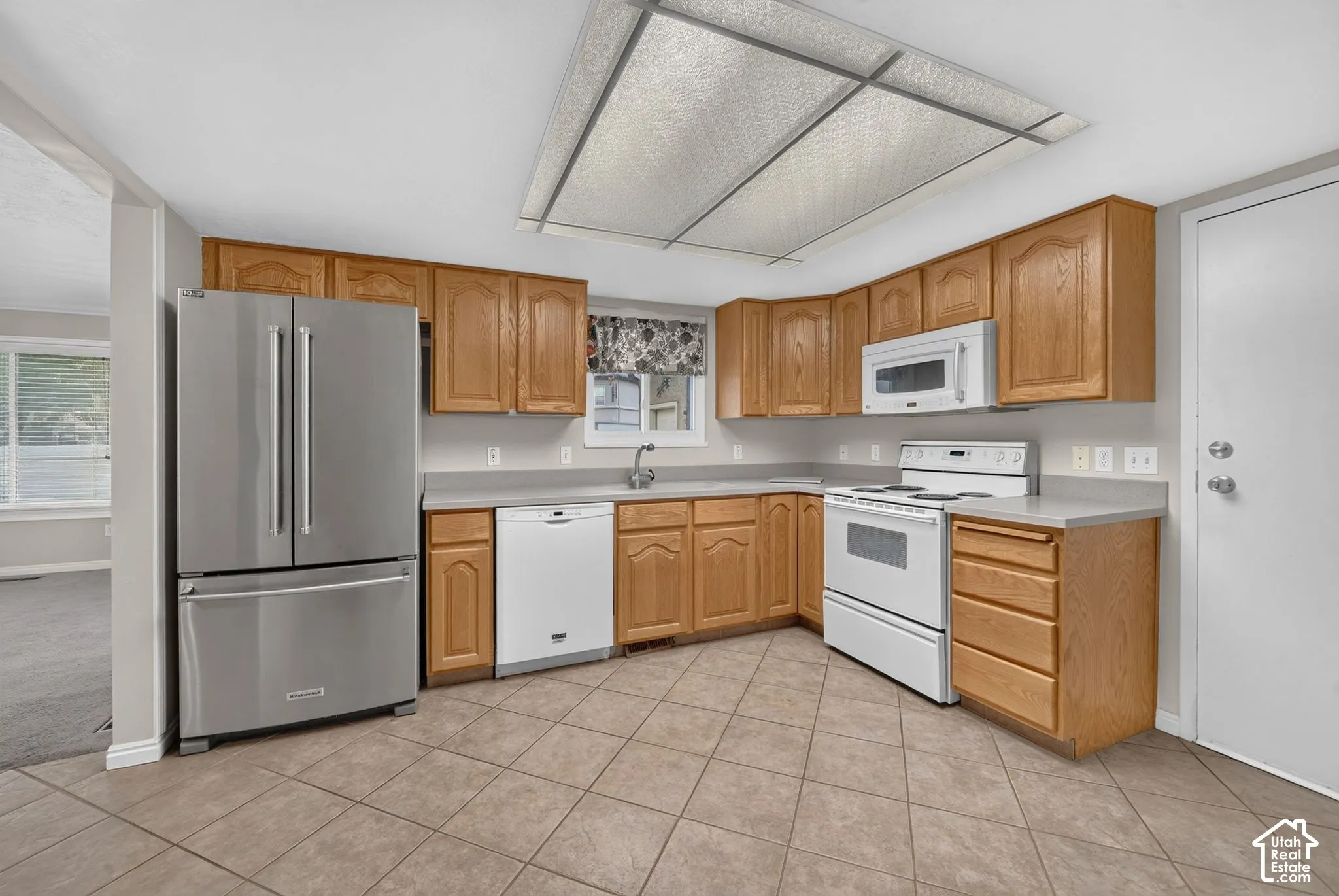 Kitchen featuring natural wood cabinetry, solid surface countertops, tile flooring, stainless steel French-door refrigerator, and white appliances