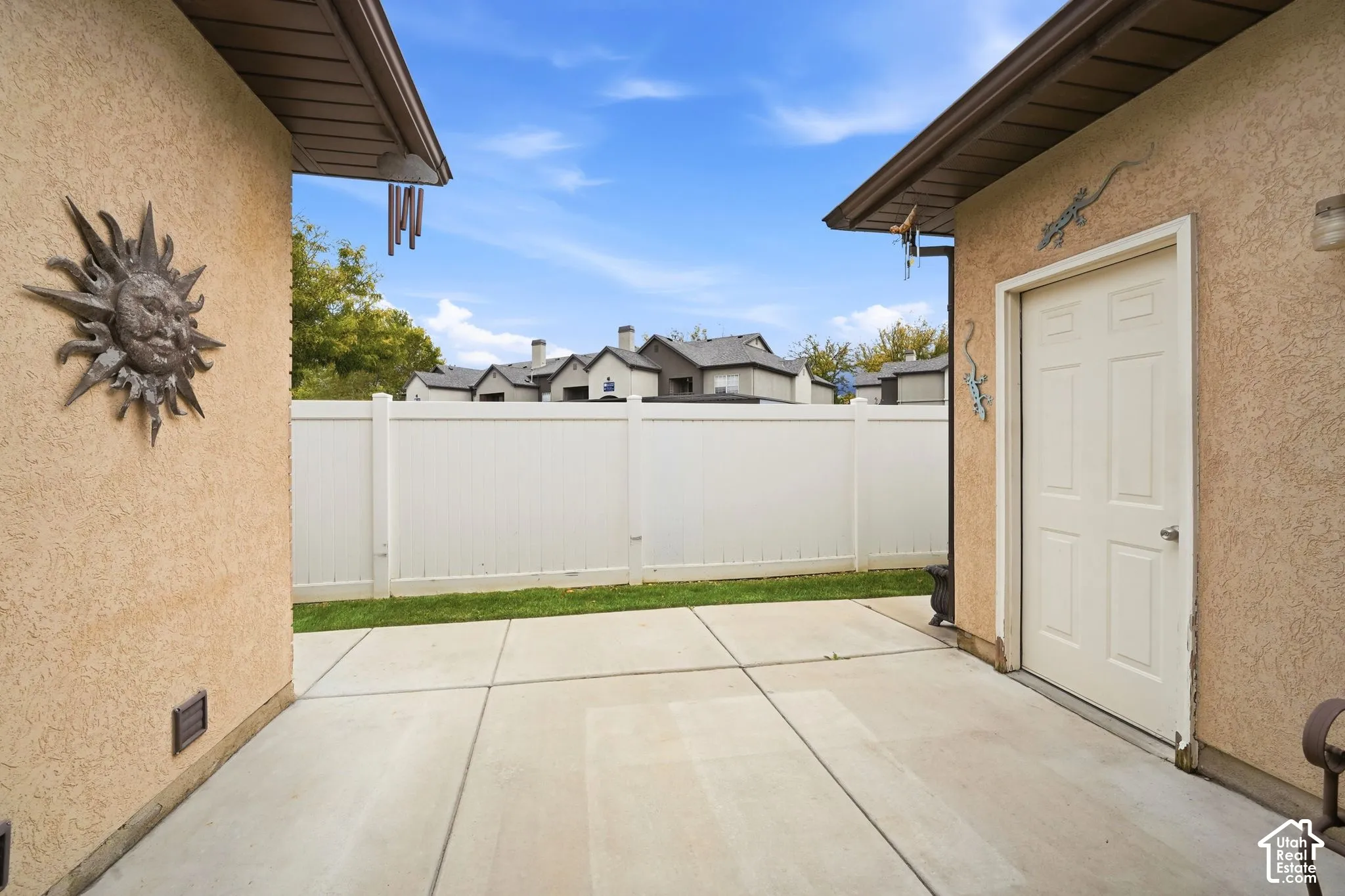 Concrete patio featuring stucco exterior walls, an enclosed yard with a white privacy fence, and an exterior door