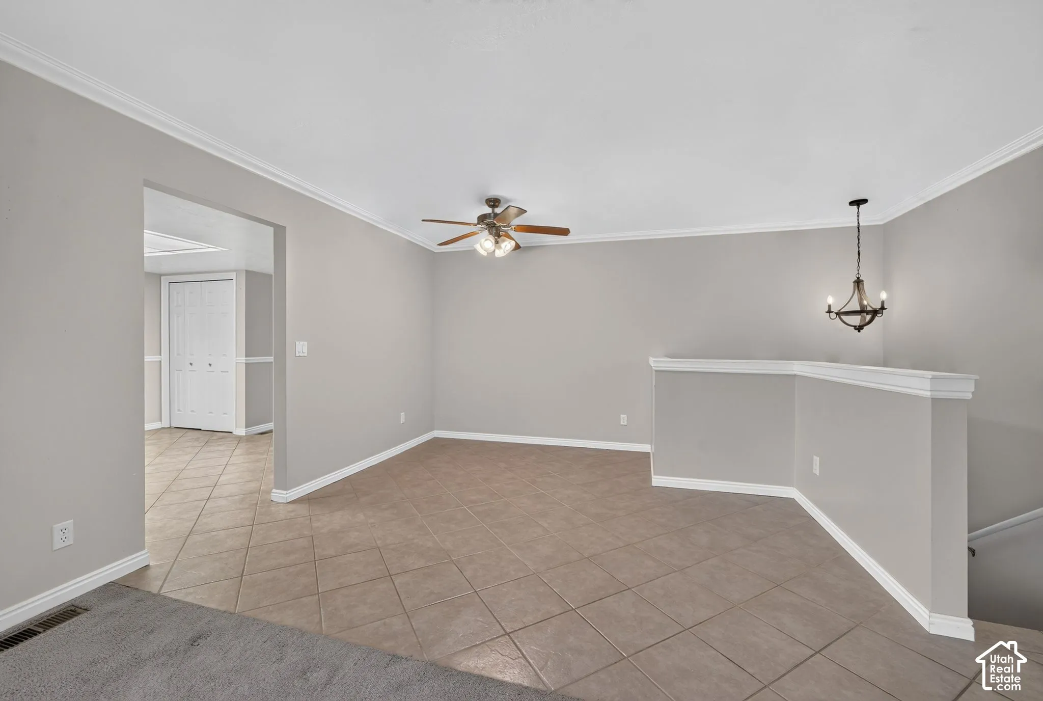 Neutral interior space featuring diagonal ceramic tile flooring, crown molding, a multi-blade ceiling fan with integrated lighting, and a wrought-iron style chandelier