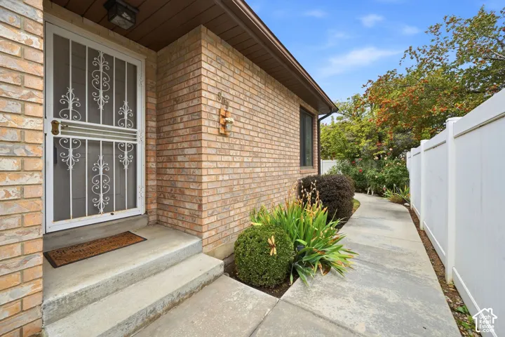 Brick exterior facade featuring a concrete walkway, white privacy fencing, and metal security storm door