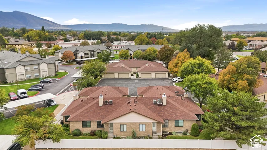 Aerial perspective featuring a multi-unit complex with shingle roofing, brick and stucco siding, private garages, and a mountain backdrop