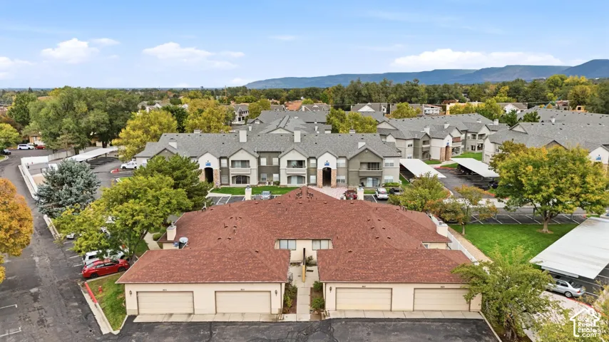 Multi-building residential complex featuring shingled hip roofs, stucco siding, detached garage structures, covered parking carports, and mature trees against a mountain backdrop