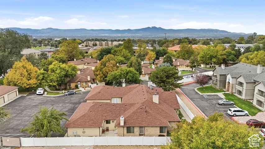 Aerial perspective of the property featuring a multi-pitched shingle roof, exterior chimneys, a private concrete patio, and fenced perimeter, set against a backdrop of distant mountain ranges