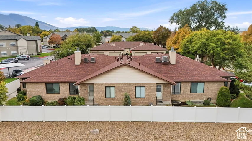 Multi-unit brick exterior featuring a multi-pitched roof, white vinyl fencing, and mountain backdrop